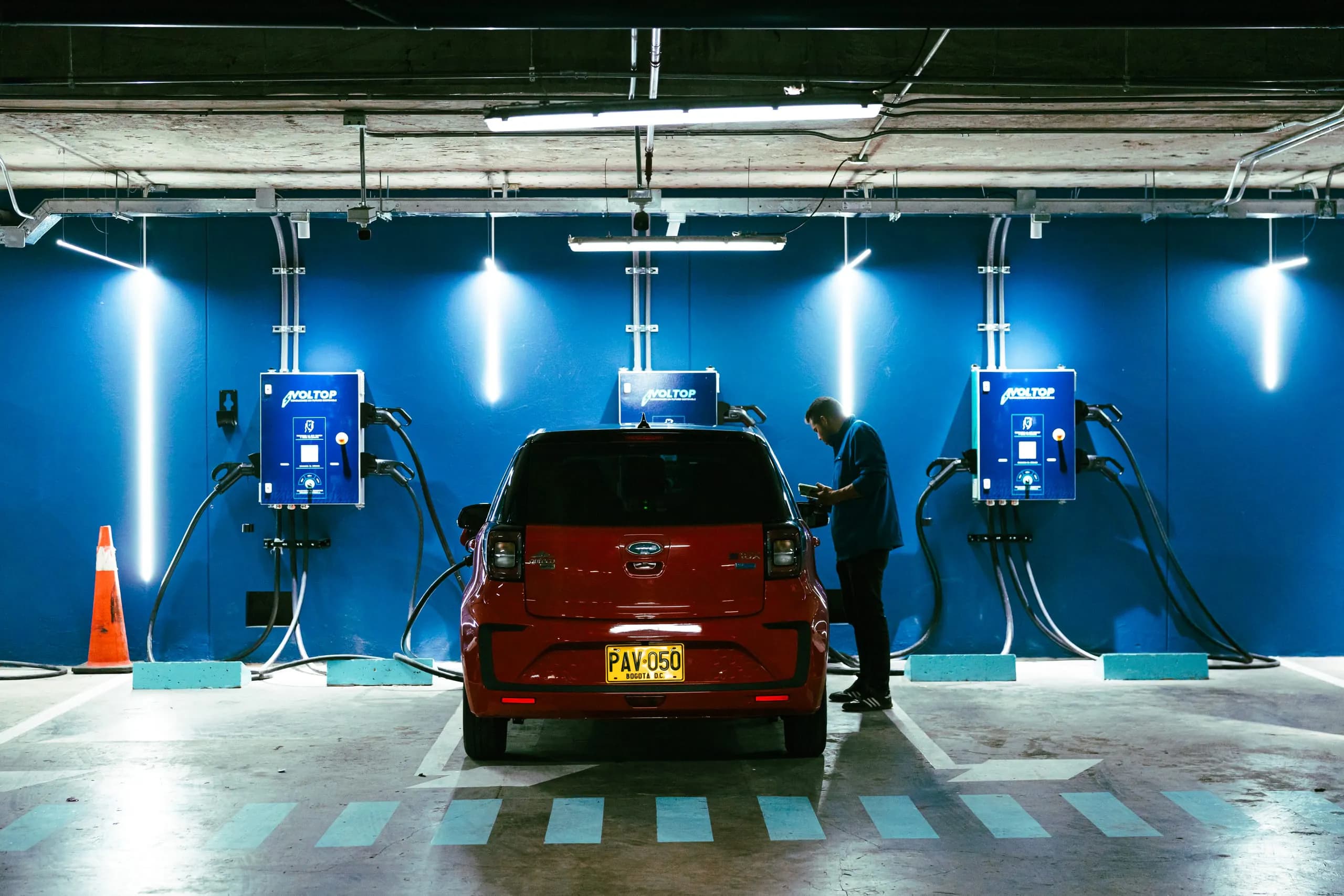 Three Voltop chargers in the Grand Hyatt covered parking area, with an electric vehicle plugged in and a person starting the charge